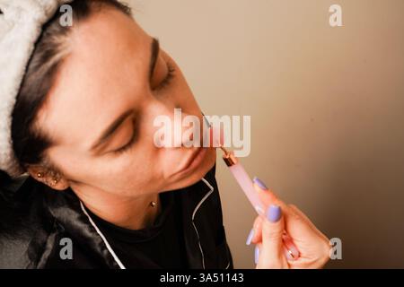 Anti-Aging-Hautmassage, Nahaufnahme. Schönheitsbehandlungen zu Hause. In einem Haarreif, der ihr Haar hält, gibt sich ein Mädchen eine Gesichtsmassage mit Gouache Stockfoto