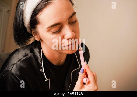 In einem Haarreif, der ihr Haar hält, gibt sich ein Mädchen eine Gesichtsmassage mit einem Gouachestein. Eine Gesichtsmassage in den Händen einer Frau. Anti-Aging Stockfoto