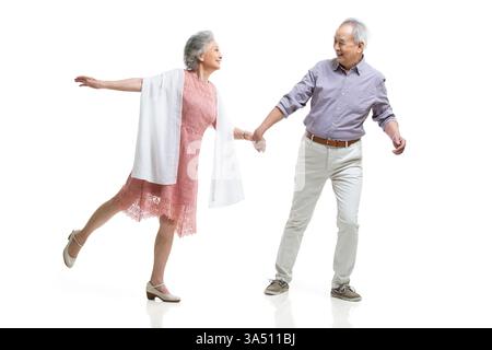 Fröhliches chinesisches Seniorenpaar, das Hände hält und zusammen in einem Studio mit weißem Hintergrund läuft. Das Bild bietet Kopierraum für Schlagzeilen und ist somit vielseitig für Pensions- und Wellnesskampagnen geeignet. Ein warmes, liebevolles Porträt, das Langlebigkeit und Happy Aging unterstreicht und für Familien- und Lifestyle-Marken geeignet ist. Stockfoto