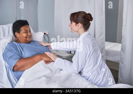 Seitenporträt einer pflegenden Krankenschwester, die eine ältere Patientin in einem Krankenhausbett unterstützt. Diese Gesundheitsszene hebt Mitgefühl, Komfort und Patientenversorgung in einem klinischen Umfeld hervor. Stockfoto