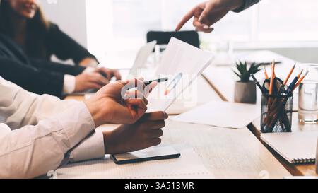 Verschiedene junge Teams arbeiten an einem Geschäftsprojekt mit Finanzberichten und Diagrammen zusammen. Die moderne Büroszene legt Wert auf Teamarbeit, Strategie und professionelle Zusammenarbeit. Stockfoto