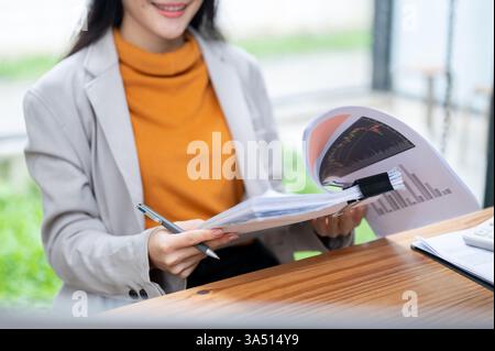 Nahaufnahme einer asiatischen Geschäftsfrau, die Finanzberichte an ihrem Schreibtisch liest. Sie wirkt fokussiert und professionell und eignet sich für Unternehmens- und Finanzinhalte. Verwenden Sie dieses Bild für Überschriften zu Marktanalysen, Buchhaltung und Geschäftsberichten, wobei der Kopierbereich verfügbar ist. Stockfoto