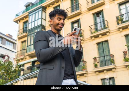 Tiefwinkelansicht eines modernen arabischen Versicherungsagenten mit Smartphone im Freien. Ein professionelles, kundenorientiertes Image, das sich für Finanzdienstleistungen, Versicherungen und Geschäftskommunikation eignet. Stockfoto