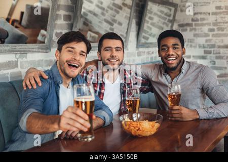 Freunde genießen Bier in einer Bar, ruhen sich aus und schauen in die Kamera. Diese lebhafte Gruppenszene fängt Gastfreundschaft, Nachtleben und soziale Kontakte in einer zwanglosen Bar-Umgebung ein. Stockfoto