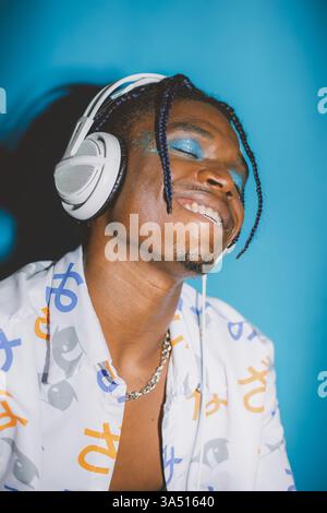 Afroamerikaner, der Kopfhörer trägt, genießt Musik vor blauem Studiohintergrund. Ideal für Musik-, Unterhaltungs- und Technologiekampagnen. Stockfoto