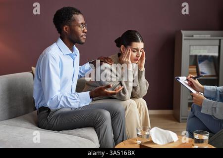 Ein verheiratetes Paar besucht einen Familienpsychologen, um Beziehungsprobleme in einem bequemen Sofa zu besprechen. Die Szene konzentriert sich auf Therapie, Kommunikation und Unterstützung für geistiges Wohlbefinden. Ideal für Kampagnen über Paarberatung und Beziehungsgesundheit. Stockfoto
