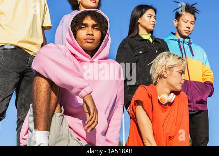 Ein Afroamerikaner in einem Hoodie sitzt draußen mit Freunden und lehnt sich bei einem zwanglosen Treffen im Park auf ein Knie. Die entspannte, urbane Atmosphäre passt zum Lebensstil junger Menschen und zu Freundschaftskampagnen. Ideal für Bekleidung, Turnschuhe und Streetwear-Marketing. Stockfoto
