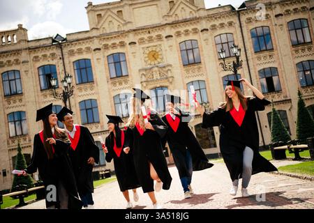 Fröhliche College-Absolventen feiern ihre akademischen Leistungen draußen an einem sonnigen Campus-Tag Stockfoto