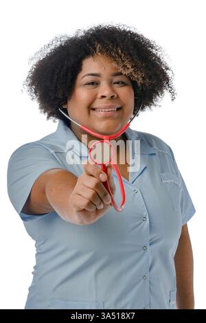 Übergroße hispanische Ärztin mit einem lockigen Afro in blauer Uniform, mit einem Stethoskop vor weißem Atelierhintergrund. Dieses professionelle Porträt im Gesundheitswesen unterstützt Krankenhaus, Klinik und medizinische Kampagnen. Es fördert auch die Vielfalt in der Medizin und weibliche Führungsqualitäten. Stockfoto