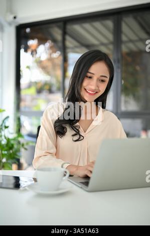 Die charmante und erfolgreiche asiatische Geschäftsfrau der Millennials arbeitet an einem Laptop in einem modernen Büro. Sie tippt auf einer Tastatur und konzentriert sich auf geschäftliche Aufgaben an einem modernen Arbeitsplatz. Dieses Bild eignet sich perfekt für Darstellungen zu weiblichem Unternehmertum, Führungspersönlichkeit und professionellen Frauen in Thailand. Stockfoto