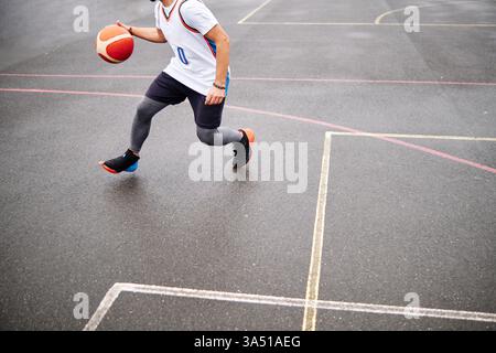 Zugeschnittenes Bild eines Mannes, der Basketball auf einem Platz im Freien spielt. Dynamische Sportanlage, geeignet für sportliches Training und Jugendsport. Der Action-Schuss betont die Bewegung und die Anstrengung auf dem Platz. Stockfoto