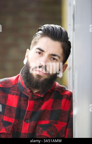 Nahporträt eines bärtigen Mannes mit Piercings, das einen auffälligen, modernen Look präsentiert. Das städtische Feeling und die stilvollen Details machen es für Mode- und Porträtfotografie geeignet. Ideal für Mode, Lifestyle und trendige urbane Themen. Stockfoto