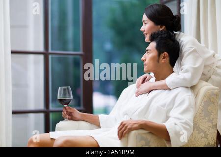 Liebevolles chinesisches Paar, das einen luxuriösen Hotelaufenthalt in Bademänteln genießt. Entspannen Sie sich in einer stilvollen Hotelsuite und teilen Sie einen Moment der Romantik und Freizeit. Stockfoto