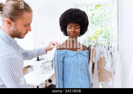 Ein vielfältiges Team von Modedesignern und Schneidern arbeitet in einem lebendigen Start-up-Studio für Bekleidung. Die multirassische Gruppe arbeitet an einer neuen Kollektion, die durch Brainstorming und Design geprägt ist und Kreativität und Teamarbeit widerspiegelt. Ideal für die Modebranche, Designstudios und Markenbilder in Boutiquen. Stockfoto