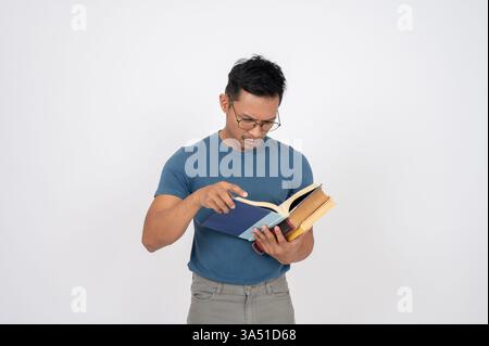 Ein asiatischer Mann in seinen 40ern auf weißem Atelierhintergrund liest ein Buch mit fokussiertem Ausdruck. Dieses Bildungs- und Lernmotiv eignet sich gut für Broschüren, Schulungen und akademische Materialien. Sie vermittelt Konzentration und Weisheit und passt zu durchdachten Kampagnen. Stockfoto
