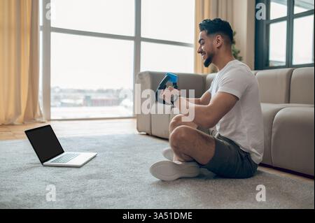 Junger Mann, der ein Heimtraining mit einem Expander in einer hellen Innenumgebung durchführt. Dieses Bild des Fitness-Lifestyles passt zu Artikeln über aktive Aktivitäten, Heimtrainings und Online-Workouts. Perfekt für Wellness- und gesunde Lebenskampagnen. Stockfoto