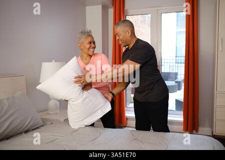 Fröhliches schwarzes Paar zu Hause, das zusammen ein Kissen auf dem Bett im Schlafzimmer arrangiert. Ein warmer Lifestyle-Moment, ideal für Wohnkultur, Paare und gemütliche Wohnkampagnen. Stockfoto