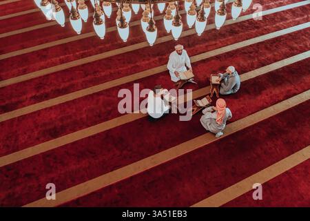 Eine Gruppe von Muslimen, die das heilige Buch des Koran in einer modernen Moschee während des muslimischen Feiertags im Ramadan lesen. Stockfoto