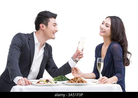 Fröhliches, junges chinesisches Paar, das ein Abendessen zusammen in einem stilvollen Ambiente genießt. Dieser kulinarische Moment unterstreicht Romantik, Feier und Zweisamkeit mit Champagner und Gourmetgerichten. Stockfoto