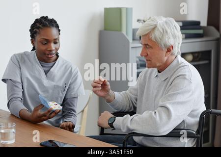 Porträt einer Krankenschwester, die einem älteren Mann in einem Altersheim einen Medikamentenplan erklärt. Die fürsorgliche Interaktion hebt die Pflege und Gesundheitsversorgung in betreuten Lebensumgebungen hervor. Geeignet für Materialien zur Altenpflege, Patientenkommunikation und Medikamentenmanagement. Stockfoto