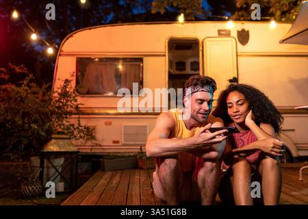 Junge Paare im Urlaub neben einem Wohnmobil, genießen eine Nacht in der Natur. Eine vom Fernweh inspirierte Szene, die perfekt für Roadtrips, Camping und Outdoor-Lifestyle geeignet ist. Ideal für Reisen, Paare und Adventure Marketing. Stockfoto