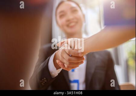 Nahaufnahme einer asiatischen Geschäftsfrau, die nach einem Treffen mit ihrem Klienten die Hand schüttelt. Ein professioneller Moment, in dem Teamarbeit, Verhandlungen und geschäftliche Zusammenarbeit im Büro hervorgehoben werden. Geeignet für Artikel zu Bewerbungsgesprächen, Kundenbeziehungen und Unternehmenserfolg. Stockfoto