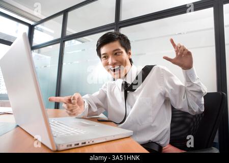 Junger chinesischer Geschäftsmann, der von einem Laptop in einem Büro überrascht wurde. Moderner, gut gekleideter Profi mit Technologie, geeignet für geschäftliche und digitale Themen. Stockfoto