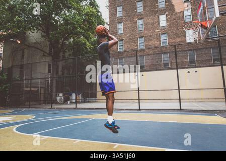 Junger afroamerikanischer Basketballspieler trainiert auf einem Stadtplatz in New York City. Dieses dynamische Sportbild fängt Fokus, Trainingstempo und Energie im Straßenbasketball ein. Stockfoto