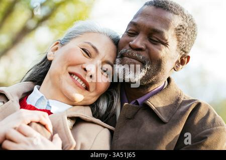 Das Geschichtenerzählbild eines multiethnischen Seniorenpaares, das verliebt ist. Sie teilen eine warme Umarmung im Freien, strahlen Zuneigung und Freude aus. Geeignet für Romantik, Altern und Lifestyle-Kampagnen. Stockfoto