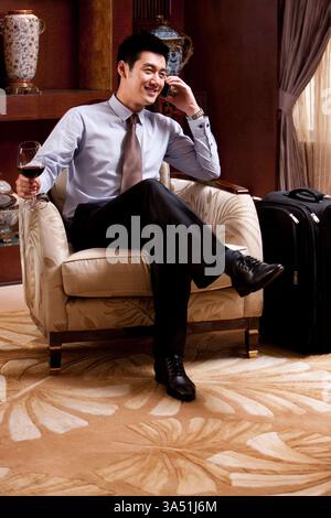 Ein junger chinesischer Geschäftsmann benutzt ein Mobiltelefon in einem Hotel. Diese hochmoderne Szene eignet sich für Geschäftsreisen, Technologie oder Unternehmenskommunikation. Stockfoto