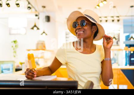 Porträt einer Schwarzen Frau, die im Sommer in einem Geschäft ein Mangoeis isst. Ideal für Lifestyle, Einzelhandel und kulinarische Momente. Stockfoto
