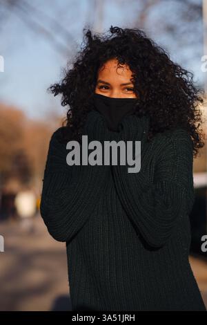 Porträt einer Frau mit Gesichtsmaske, die draußen auf einer städtischen Straße steht. Dieses Bild zeigt den neuen normalen Lebensstil und den Schutzstil in einer Stadt. Ideal für Gesundheits-, Urban Living- und Street Fashion-Kampagnen. Stockfoto