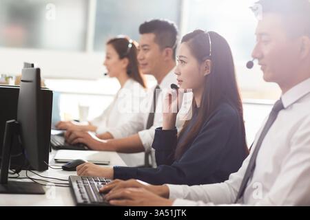 Chinesische Callcenter-Agenten arbeiten in einem hellen Büro mit Headsets zusammen. Die Szene beleuchtet Kundenservice, Teamarbeit und professionelle Kommunikation. Perfekt für Artikel über Outsourcing, Call Center und Serviceindustrie in China. Stockfoto