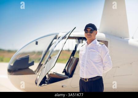 Ein chinesischer Hubschrauberpilot steht neben einem Hubschrauber und projiziert Professionalität in der Luft- und Raumfahrt. Das Porträt zeigt Karrieren in der Luftfahrt, Technologie und moderne Industrie. Nützlich für Nachrichten, Branchen und Schulungsinhalte zu Piloten und Flug. Stockfoto