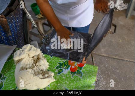 Von oben schneidet eine anonyme Frau in lässigem Outfit und Schürze frischen Rohteig in einer Bäckerei. Der hohe Blickwinkel betont die Zubereitung von Bäckerei und Lebensmittelhandwerk. Geeignet für kulinarische, gastronomische und handwerkliche Backwaren. Stockfoto