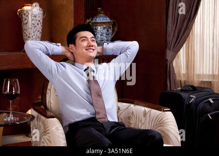 Stilvoller chinesischer Geschäftsmann in luxuriöser Hotelumgebung, sitzen und mit Zuversicht nach vorne schauen. Geeignet für Geschäftsreisen, Hospitality und Executive Lifestyle Kampagnen. Stockfoto
