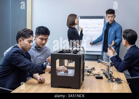 Selbstbewusste chinesische Designer arbeiten in einem modernen Büro an einem 3D-Drucker zusammen. Zeigt Kreativität, Design und Innovation in Technologie und Fertigung. Hervorragend geeignet für Funktionen im 3D-Druck, Engineering-Teams und zukunftsorientierte Geschäftsabläufe. Stockfoto
