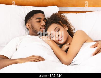 Liebevolles afroamerikanisches Paar, das eng im Bett schläft, eine zärtliche Morgenszene. Dieses Lifestyle-Bild vermittelt Wärme, Komfort und Intimität für Kampagnen rund um Beziehungen und das Leben zu Hause. Stockfoto