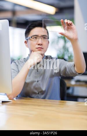 Zielgerichteter chinesischer IT-Mitarbeiter, der ein Smartphone in einem modernen Büro entwickelt. Dieses Technologiebild beleuchtet Softwareentwicklung, UI-Design und digitale Innovation. Geeignet für Artikel über mobile Apps, Karriere im technischen Bereich und IT-Kampagnen im Unternehmen. Stockfoto