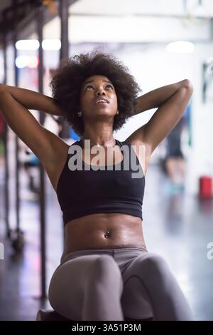 Junge afroamerikanische Frau, die Sit-UPS in einem Fitnessstudio vorführt und dabei die Kernkraft und das energetische Cardio-Training unter Beweis stellt. Ideal für Fitness-Workouts, Fitness-Motivation und gesundes Leben Kampagnen. Die Szene vermittelt Entschlossenheit in einer modernen Indoor-Trainingsumgebung. Stockfoto