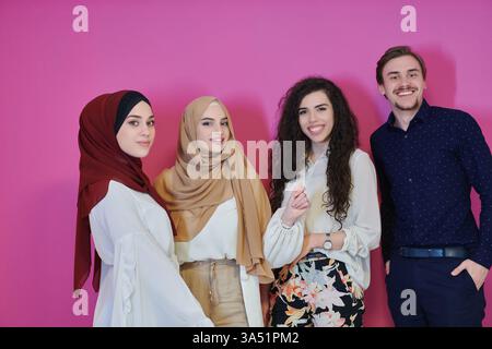 Fröhliches Porträt einer vielfältigen Gruppe von Muslimen, die Ramadan repräsentieren, darunter ein Mann und drei Frauen, die einen modernen Hijab tragen. Sie stehen zusammen vor einem rosafarbenen Hintergrund und strahlen Wärme und Zweisamkeit aus. Ideal für Ramadan, religiöse Feste und verschiedene Lifestyle-Kampagnen. Stockfoto