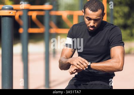 Outdoor-Porträt eines sportlichen Mannes, der seine Smartwatch nach einem Workout überprüft. Das fängt Fitness-Technologie, Fortschritt und gesundes Leben in einer hellen Umgebung im Freien ein. Ein vielseitiges Image für Fitness, Training und aktive Lifestyle-Themen. Stockfoto