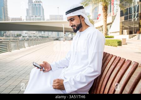 Porträt eines Mannes aus dem Nahen Osten, der draußen in Dubai eine Kandora trägt. In traditioneller emiratischer Kleidung strahlt er eine moderne, professionelle Atmosphäre aus. Geeignet für Reise-, Kultur- und Geschäftsreisen in den VAE. Stockfoto