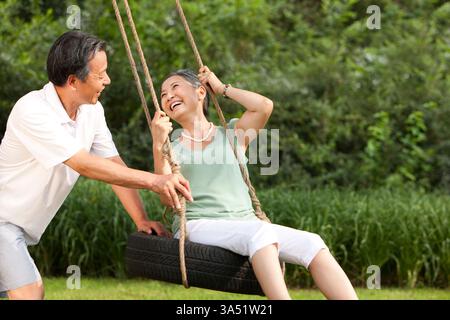 Fröhliches chinesisches Seniorenpaar, das draußen eine Schaukel genießt. Dieses warme Lifestyle-Bild vermittelt Energie, Glück und Zweisamkeit – ideal für Pensionär-, Familien- oder Reisekampagnen. Stockfoto