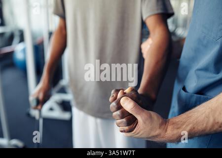 Nahaufnahme eines Arztes, der einen Patienten unterstützt, während er nach einer schweren Verletzung wieder laufen lernt. Das Bild ist ideal für Artikel über Rehabilitation, Physiotherapie und mitfühlende medizinische Versorgung in einem klinischen Umfeld. Stockfoto