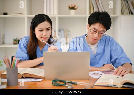 Fokussierte asiatische Medizinstudenten studieren gemeinsam in einer Bibliothek, recherchieren medizinische Informationen und bereiten sich auf Prüfungen vor. Eine Teamwork- und Bildungsszene mit Schwerpunkt auf Gesundheitstraining und medizinische Ausbildung. Ideal für Lehrmaterialien, medizinische Programme und studentische Lebensmerkmale. Stockfoto