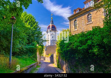 Enge Straße mit Steinzaun und grünen Pflanzen, Straßenlaterne und Turm der Kathedrale La Cathédrale Saint-Jean in der Altstadt von Besancon, La boucle Stockfoto