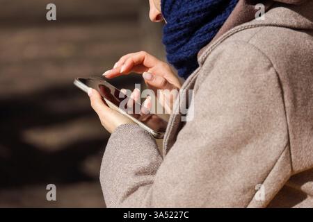 Smartphone in weiblichen Händen, Frau, die im Frühjahr auf der Straße in der Stadt ihr Handy benutzt Stockfoto
