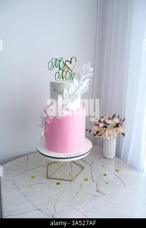 Eine rosa-weiße Hochzeitstorte mit einem grünen Blatt oben und den Worten "Mr. Und Mrs." darauf Stockfoto