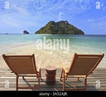 Romantische Ecke am Strand. Zwei zusammenklappbare Holzstühle und ein kleiner Beistelltisch. Durch das smaragdgrüne Meerwasser sichtbarer feiner gelber Sand Stockfoto